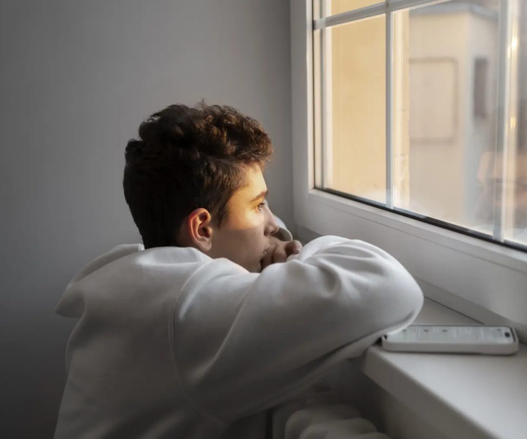 Foto de archivo de un adolescente mirando por la ventana.meteleva/freepik