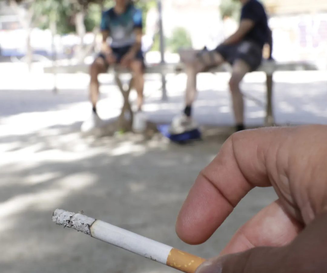 Imagen de recurso de dos jóvenes sentados en un banco con una persona fumando cerca.JORGE PARÍS