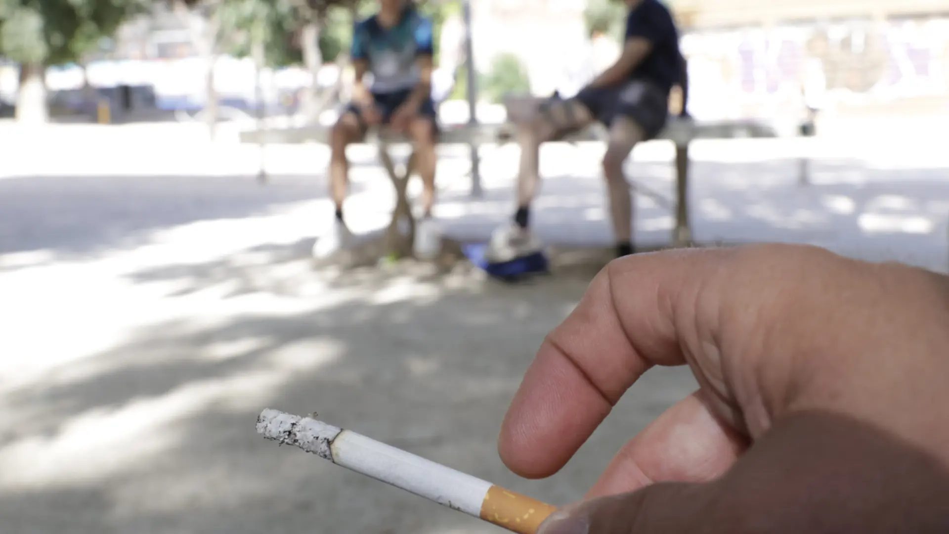 Imagen de recurso de dos jóvenes sentados en un banco con una persona fumando cerca.JORGE PARÍS